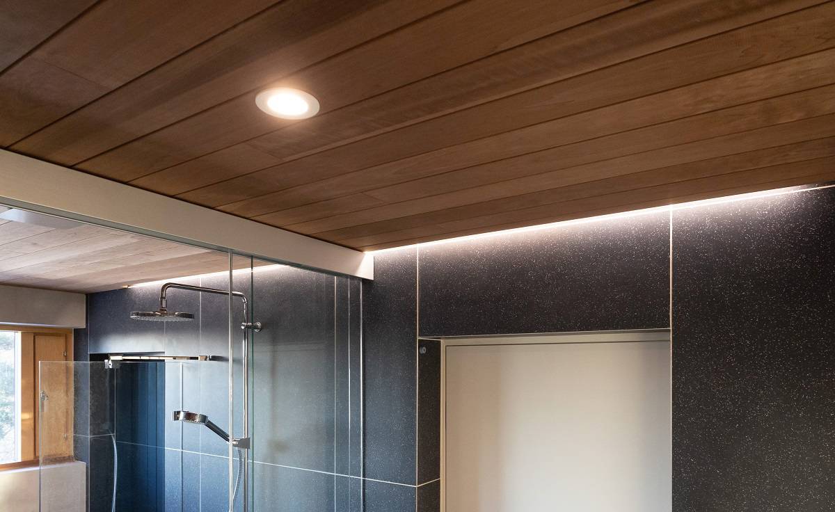 L'espace sauna est éclairé par des spots encastrés dans le plafond et des bandes LED indirectes le long du mur à côté du plafond.